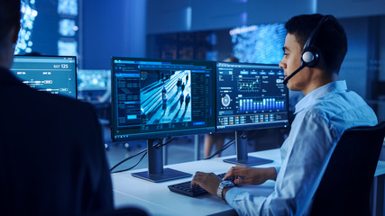 Wall Mural - Confident Male Data Scientist Works on Personal Computer Wearing a Headset in Big Infrastructure Control and Monitoring Room. Surveillance Tracking Shot of People Walking on City Streets