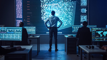 Fototapete - Project manager Stands Next to Big Screen with Neural Network. Team of Professional Computer Data Science Engineers Work on Desktops in a Dark System Control and Monitoring Telecommunications Office.