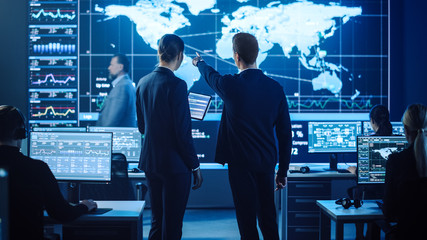Project Manager and Computer Science Engineer Talking while Using A Digital Tablet Computer. Telecommunications Company System Control and Monitoring Office Room with Working Specialists.