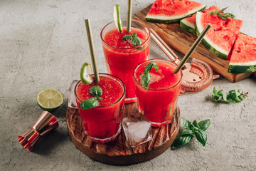 Wall Mural - Watermelon lemonade with lime and fresh basil leaves on concrete background. Refreshing summer drink