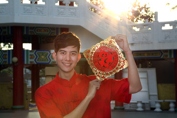 Young south east asian Chinese man traditional costume holding new chinse new year greeting outdoors at temple