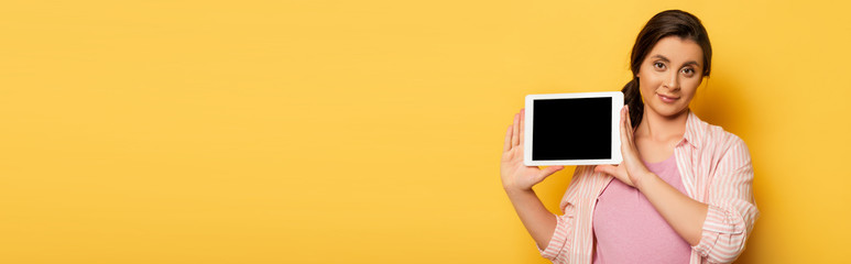 Wall Mural - panoramic shot of pregnant woman showing digital tablet with blank screen on yellow