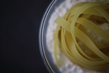 Wall Mural - Pasta on the table with spices and vegetables. Noodles with vegetables for cooking on a black stone background.