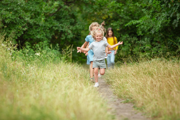 Wall Mural - Carefree. Kids, children running on green forest. Cheerful and happy boys and girs playing, laughting, running through green blooming meadow. Childhood and summertime, sincere emotions concept.