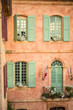Vertical close-up picture of town hall in Roussillion, Provence, France. Old historical building with orange walls and green windows. Provencal and french flags near balcony door. Travel destination