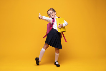 education, school, childhood, people and vision concept - smiling cute little girl with black eyeglasses showing thumbs up gesture over yellow background