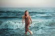 © Maryna - a girl with her hair down and in a wet sundress stands in a choppy sea with waves and smiles