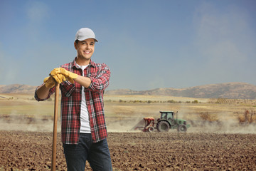 Poster - Male worker in a field with a tractor cultivating the soil in the back