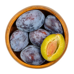 Wall Mural - Ripe European plums with cross section of one fruit in a wooden bowl. Freestone fruit with purple, violet and black skin, also called Zwetschge or Damson. Prunus domestica. Close up from above. Photo.