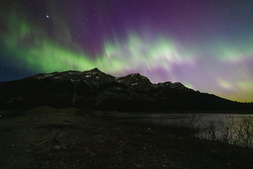 night dark sky with colourful aurora borealis dancing over a mountain