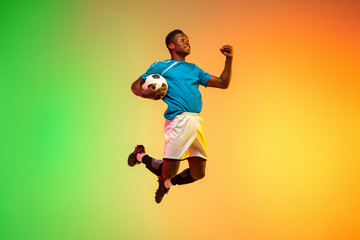 High jumping winner. Male soccer, football player training in action isolated on gradient studio background in neon light. Concept of motion, action, ahievements, healthy lifestyle. Youth culture.