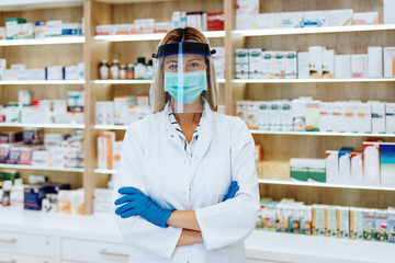 Wall Mural - Female pharmacist with protective mask on her face talking on phone while working at pharmacy. Medical healthcare concept.