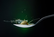 Closeup Of Green Olive With Splashing Oil On A Spoon On A Dark Background
