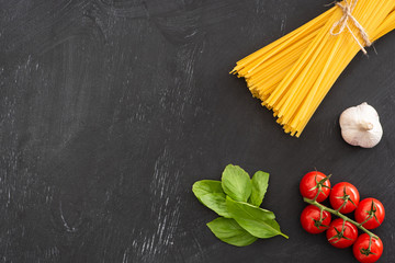 Wall Mural - top view of raw Italian spaghetti with basil leaves, tomatoes and garlic on black background