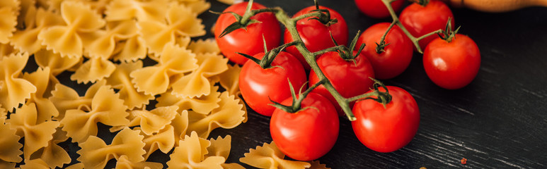 Wall Mural - raw Italian farfalle with tomatoes on black background, panoramic shot