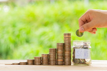 White hand man holding coin to putting in Jar or glass bottle for saving with nature green background. Saving money, Saving concept