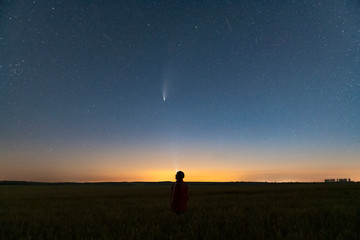 Wall Mural - silhouette of a man standing at night in a field outside the city. starry night sky with comet neowi