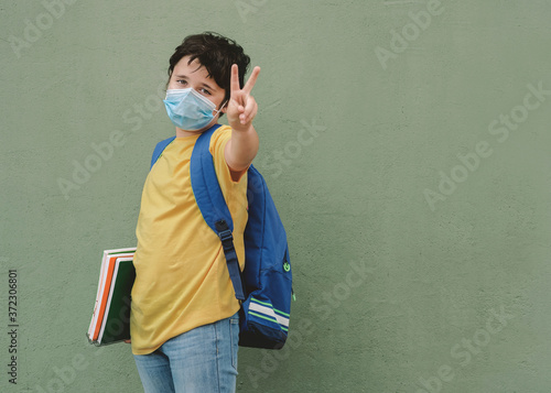 covid-19,kid with medical mask and backpack going to school doing victory sign