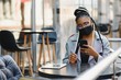 © Serhii - education, healthcare and pandemic concept - african student girl wearing face protective medical mask for protection from virus disease with laptop at cafe