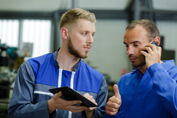 mechanic using a phone while colleague shows him tablet