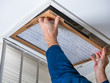 Leinwandbild Motiv Man replacing dirty HVAC air filter in ceiling vent. Home air duct system maintenance for clean air.