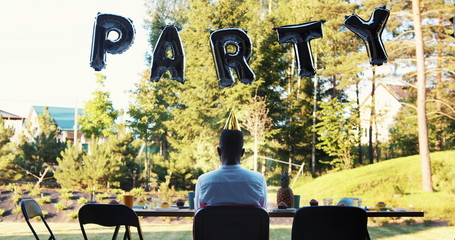 Rear view sad lonely African young man sitting alone celebrating birthday party at home on self isolation slow motion.