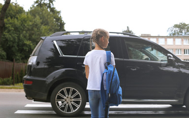 The girl crosses the street at a pedestrian crossing. The child goes to school.
