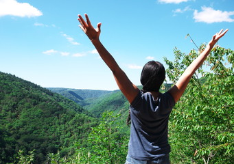 Black woman seen from behind, raising her arms and breathing the air of nature