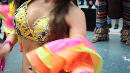 Wall Mural - The celebration of the Brazilian carnival in Moscow. Beautiful girl bright colorful carnival costume decorated with rhinestones dancing samba against the background of a yellow building. Half-naked