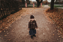 Little Girl Standing On The Road With Autumn Leaves