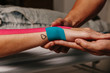 © MyMicrostock/Stocksy - Physiotherapist using kinesiotaping techniques on woman arm