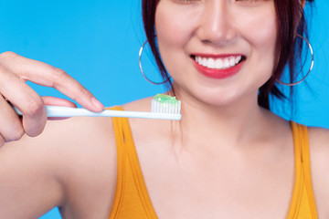 Hands of smile young woman holding toothbrush with toothpaste over isolated blue background. Healthy care tooth concept.