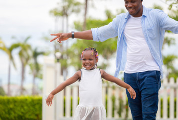 Wall Mural - Cheerful african american girl playing outdoor with her father in the park