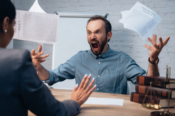 selective focus of angry and bearded man screaming while throwing in air documents near lawyer
