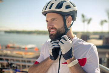 Concentrated man in sports gloves buttoning helmet