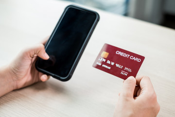 The businesswoman's hand is holding a credit card and using a smartphone for online shopping and internet payment in the office