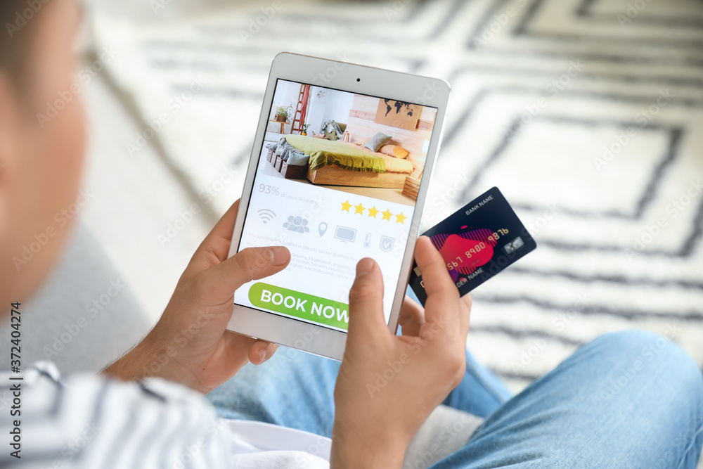 Man with tablet computer booking room in hotel online at home