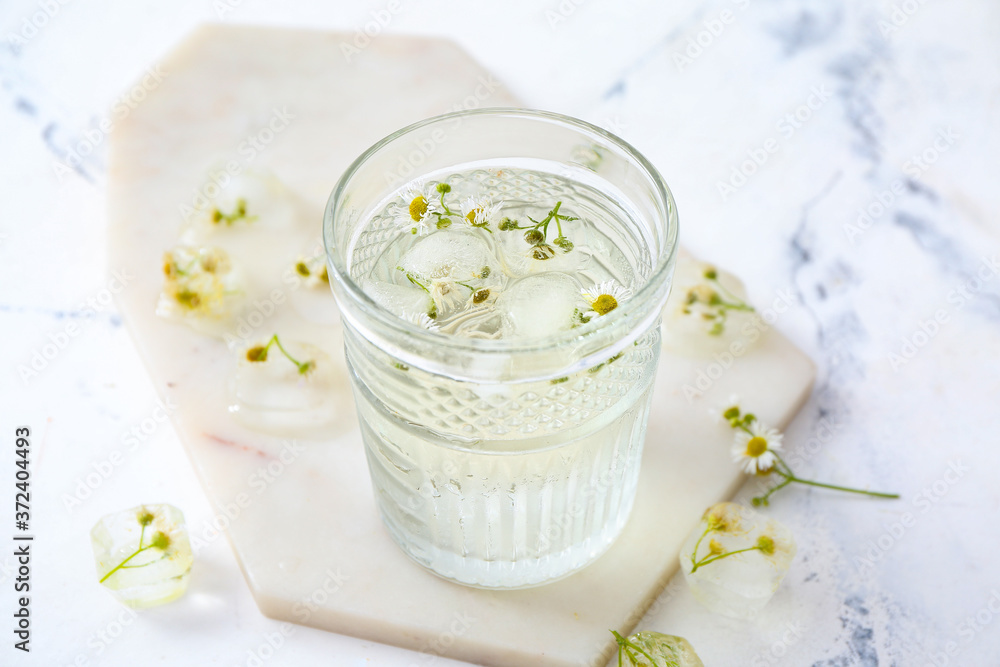 Glass with frozen flowers in ice on white background