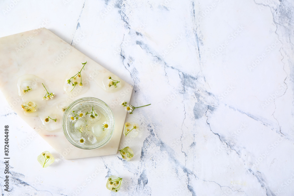 Glass with frozen flowers in ice on white background