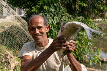 A poor fisherman showing a big Catla fish (Labeo catla) with a proud smile on his face