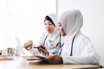 Wall Mural - Two muslim asian woman doctor working with clipboard and laptop computer on desk in hospital.healthcare and medicine