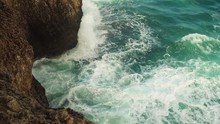 Small Waves In Green Sea Water Crashing On Rocky Shore On A Sunny Day, Slow Motion Video