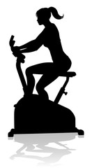 A woman in silhouette using a stationary exercise spin bike piece of gym equipment fitness machine