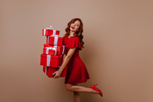 Blithesome Ginger Lady Holding Cute Christmas Gifts. Studio Photo Of Carefree Woman In Short Dress Posing With Presents.