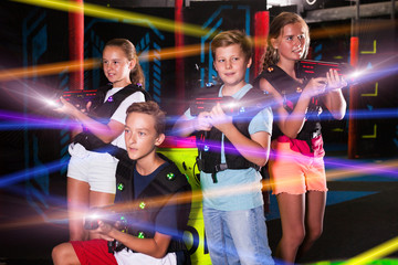  Portrait of excited teen kids with laser guns during lasertag game in dark room..