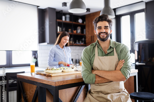 Fotografía Happy young friends loving couple chefs on the kitchen cooking.
