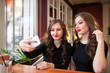© fotofrol - Two beautiful girls do selfi and drink coffee
