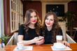 © fotofrol - Two beautiful girls drink coffee and look in the phone