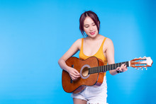 Happiness Young Woman Play Music With Acoustic Guitar On Blue Background. Portrait Cheerful Female Holding Guitar On Her Hand While Standing On Isolated Background.