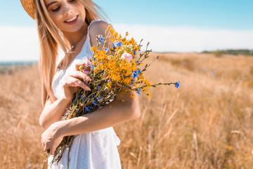 Wall Mural - selective focus of young blonde woman holding bouquet of wildflowers in meadow